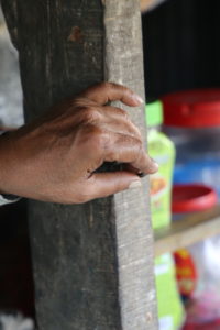 First three fingers of hand grip round, metal ring attached to wooden post, with brightly colored jars in the background.