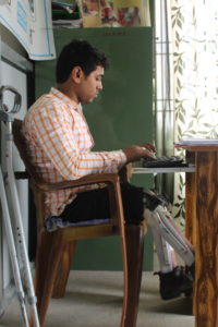 The profile of a man with bilateral orthotics sitting at his desk on a computer and working on a pull-out keyboard.