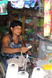 Shop seller sits in a wheelchair and hands money back to customer from inside his shop which is well stocked with items.