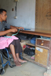 Man sits at right angle to a table raised by bricks. He is measuring some materials for cutting at the table.