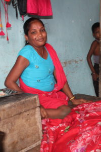 Lady with lower leg weakness prepares to use arms to get her up on bed area / lady is seen sitting inside her shop, ready to cut fabric for sewing. Her shop is at a raised height using a wide table, similar to bed height.